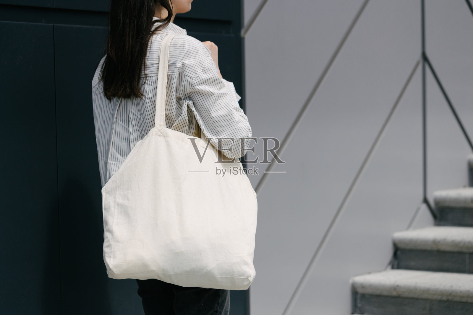 一位女性在城市中提着白色环保手提袋行走照片摄影图片