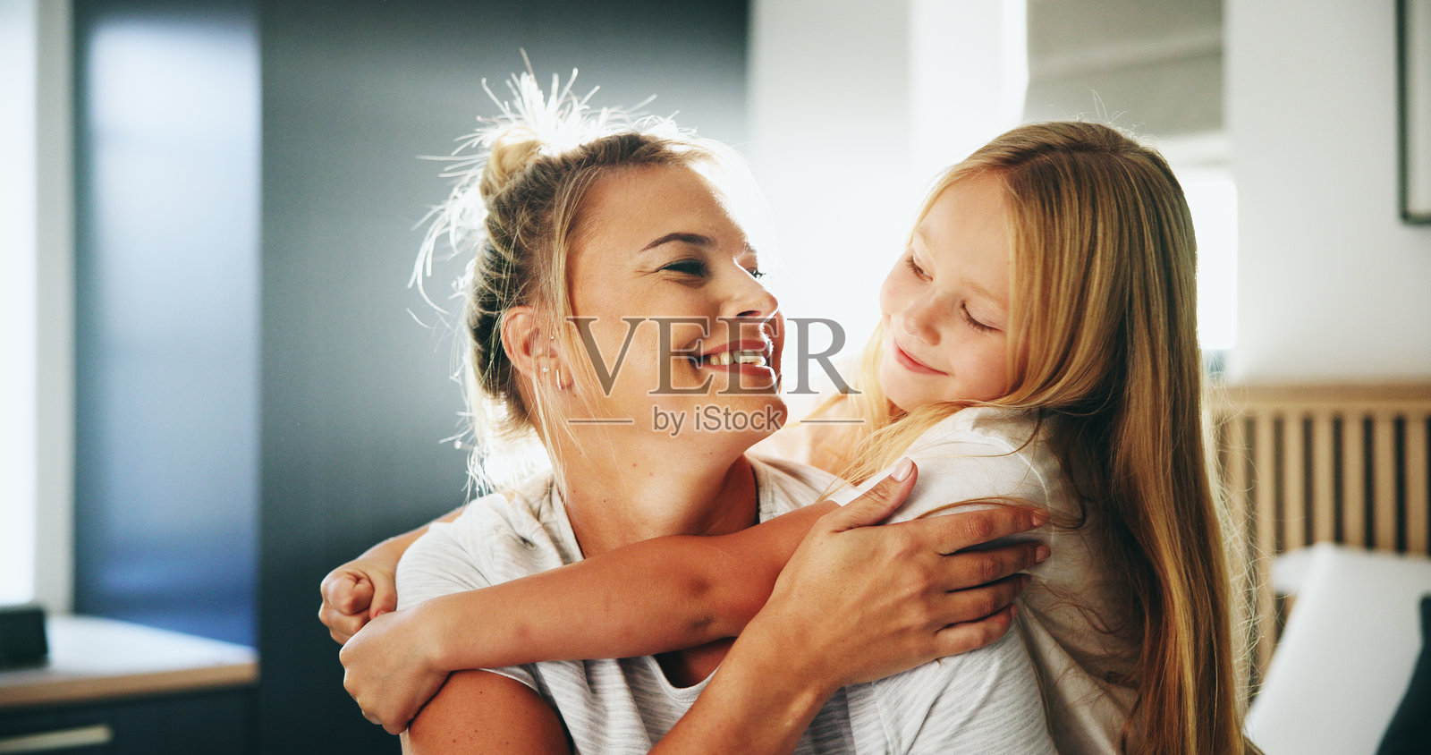 微笑的母亲在卧室里拥抱孩子，传递爱、安慰和亲密的玩耍。快乐的家庭与女孩相拥，给予支持、关爱和父母的照顾，促进孩子的成长。照片摄影图片