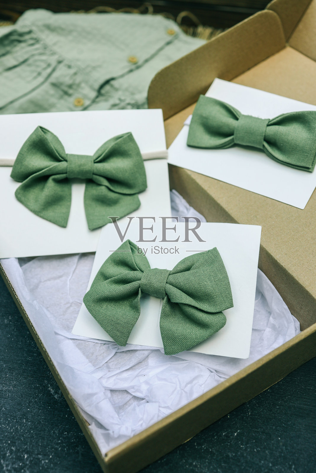 一套手工制作的绿色亚麻领结，展示在白色卡片上，装在纸板礼品盒中。适合儿童或特殊活动的优雅配饰，具有简约自然风格。照片摄影图片