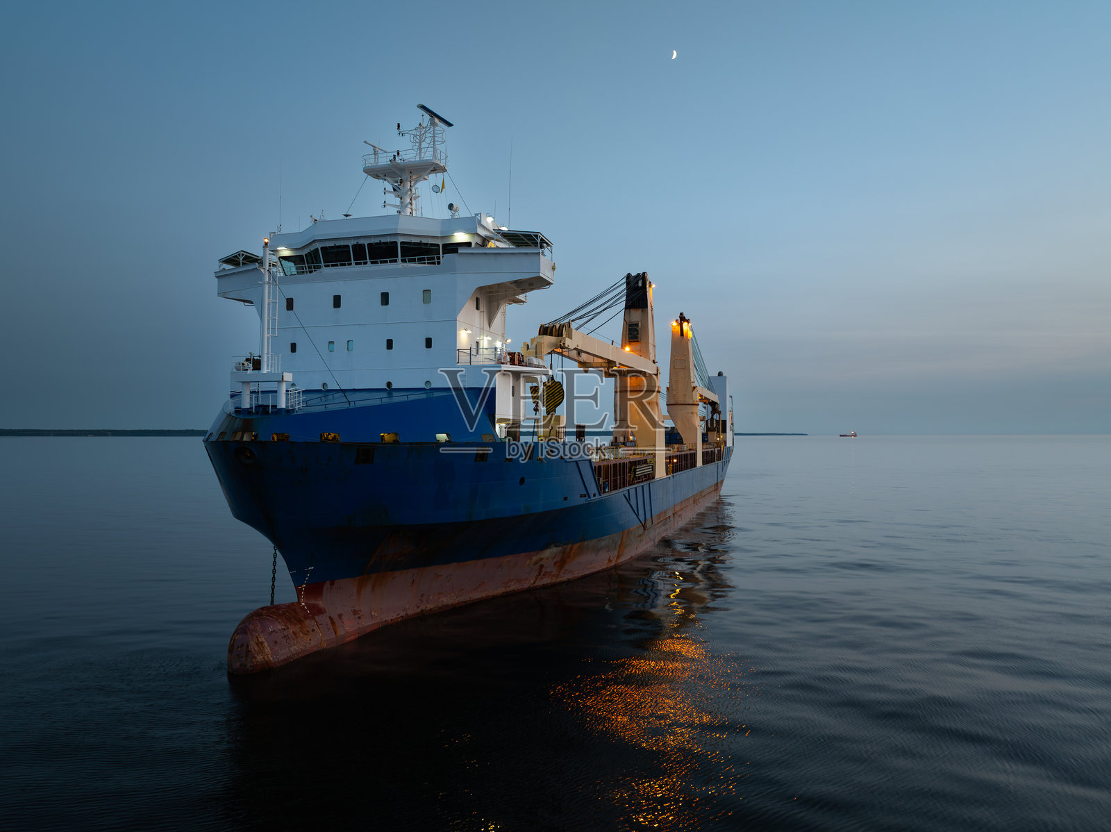 黄昏时分，波罗的海上的货船，爱沙尼亚。船只在平静的水面上亮起灯光，映衬着弯月的夜空。照片摄影图片