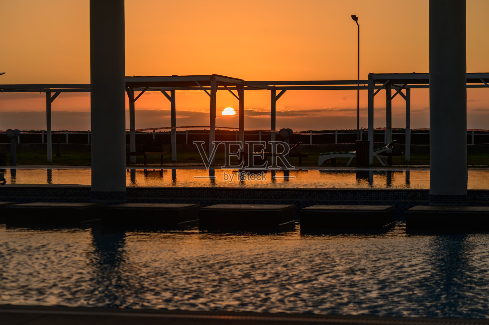 塞浦路斯度假区泳池中宁静水面上反射出鲜艳的橙色和粉色夕阳色调。照片摄影图片