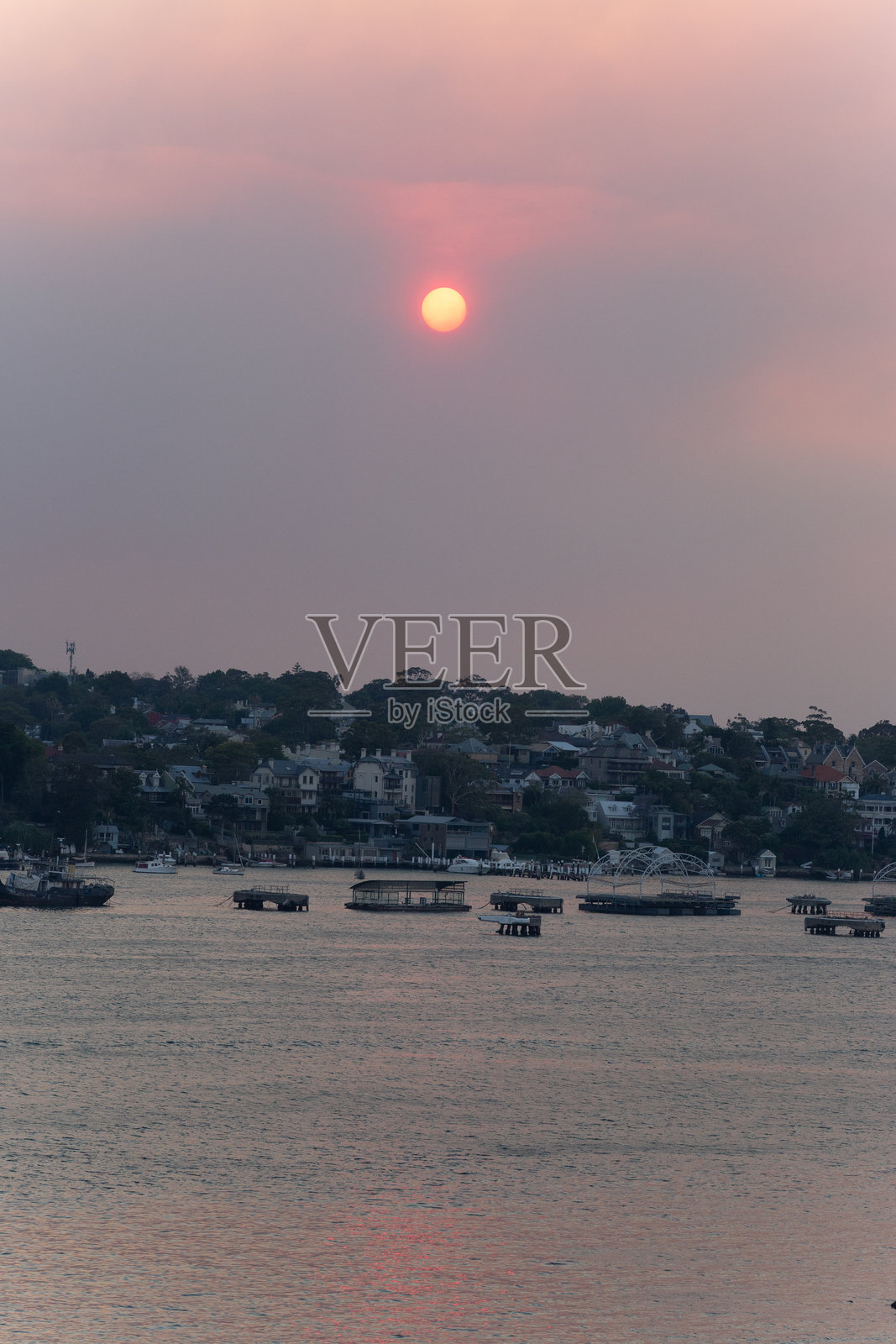 在炎热的夏季森林大火中，阳光透过浓厚的烟雾微弱地照射，映照在港口的水面上，形成了一幅令人毛骨悚然的景象。照片摄影图片