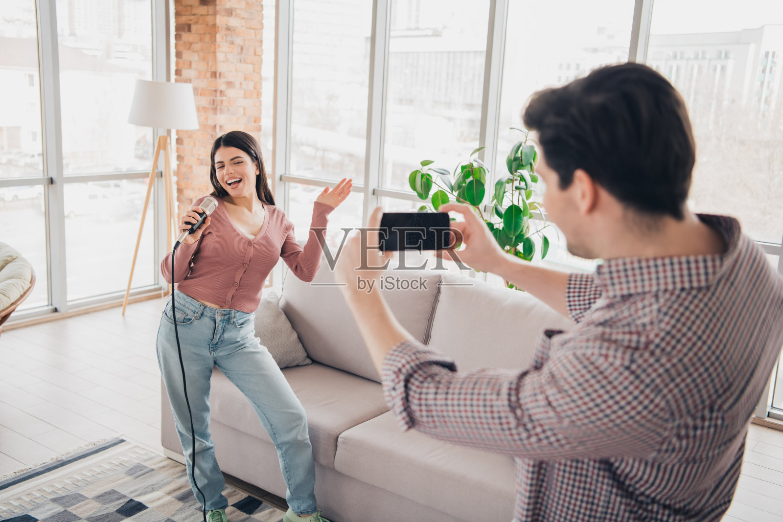 年轻情侣在现代公寓的白天享受休闲时光，唱歌并录制视频。照片摄影图片