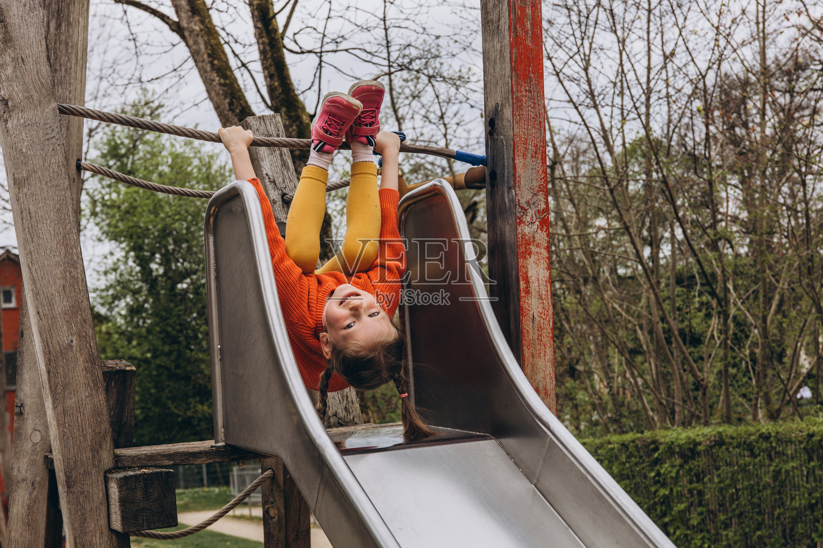孩子在游乐场的滑梯上滑下，脸上挂着灿烂的笑容，享受着户外快乐无忧的时光。照片摄影图片