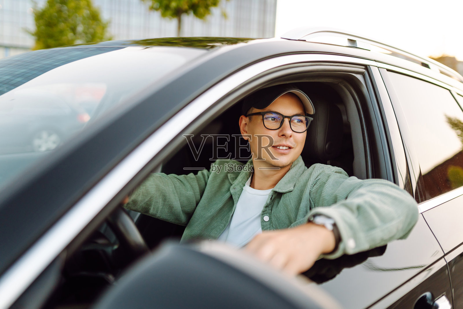 年轻男子坐在车轮后，享受阳光明媚的天气，望着窗外。照片摄影图片