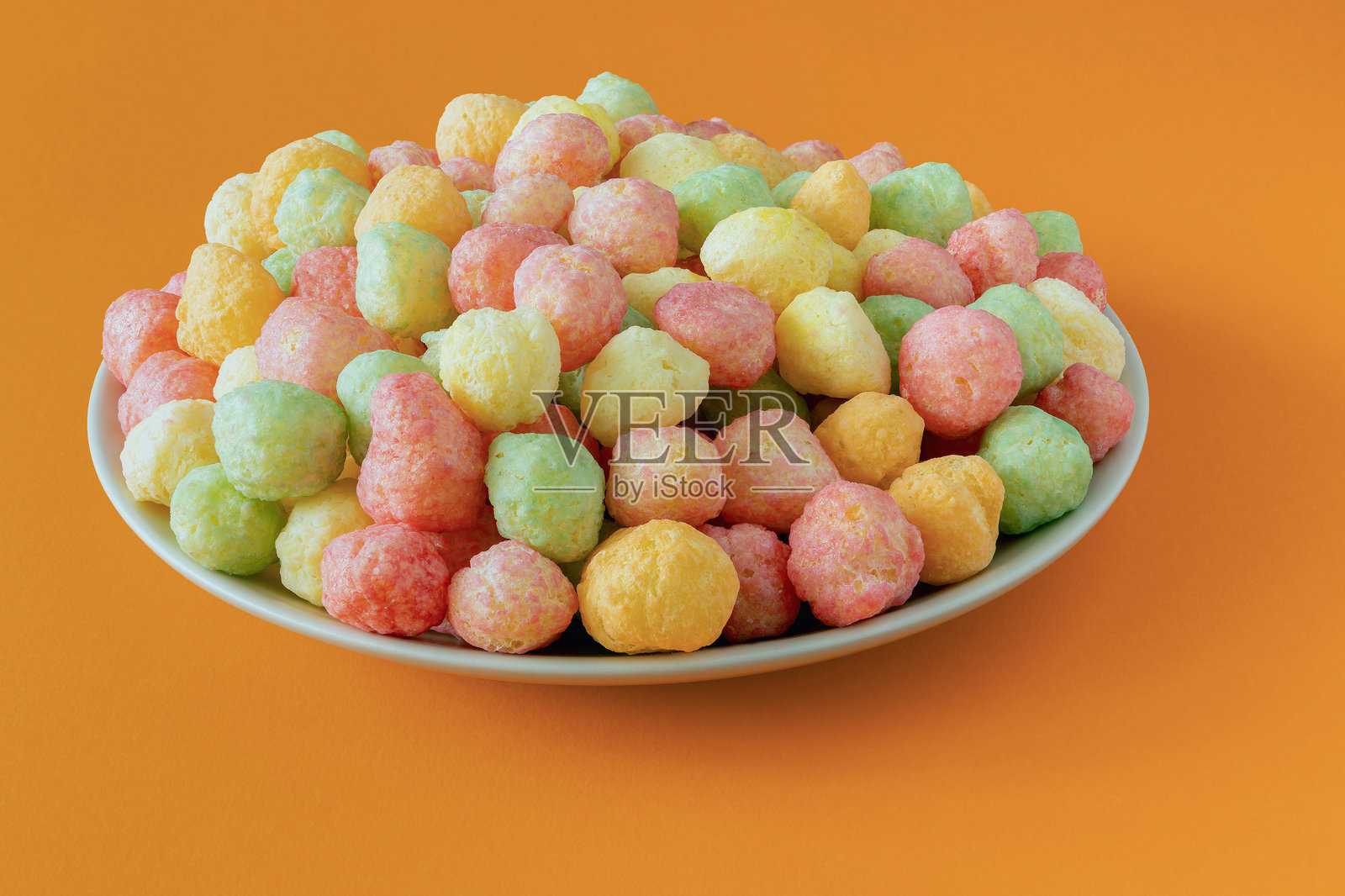 橙色背景上盘子里盛放着各种口味的玉米零食照片摄影图片