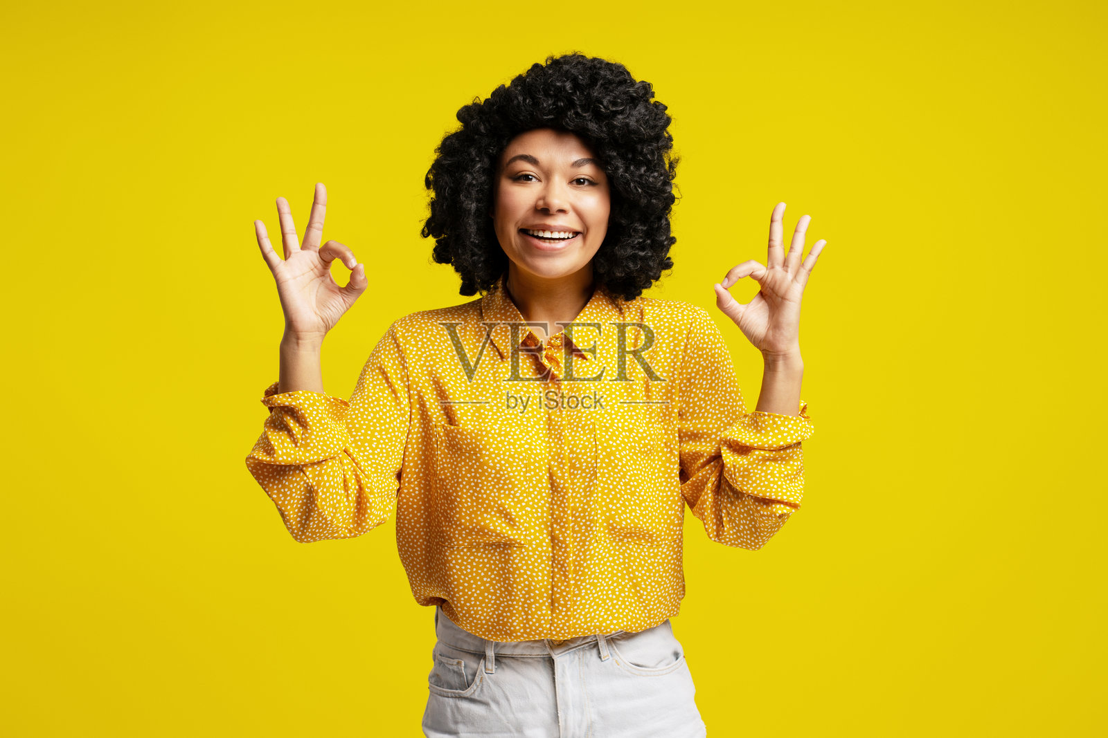 年轻女性双手做出“好”手势，面带微笑，背景为黄色。照片摄影图片