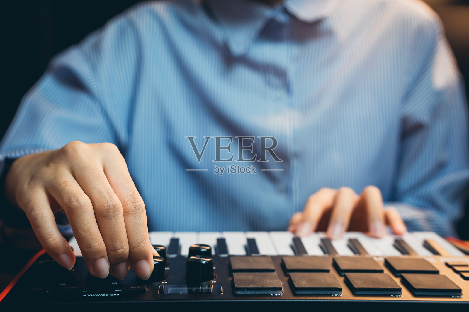 音乐制作人的概念。特写镜头展示一位音乐制作人在家庭工作室中调整MIDI键盘上的控制器。照片摄影图片