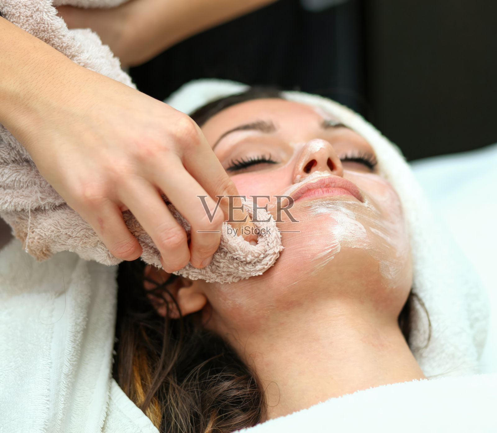 美容师用毛巾为年轻女性卸下面膜照片摄影图片