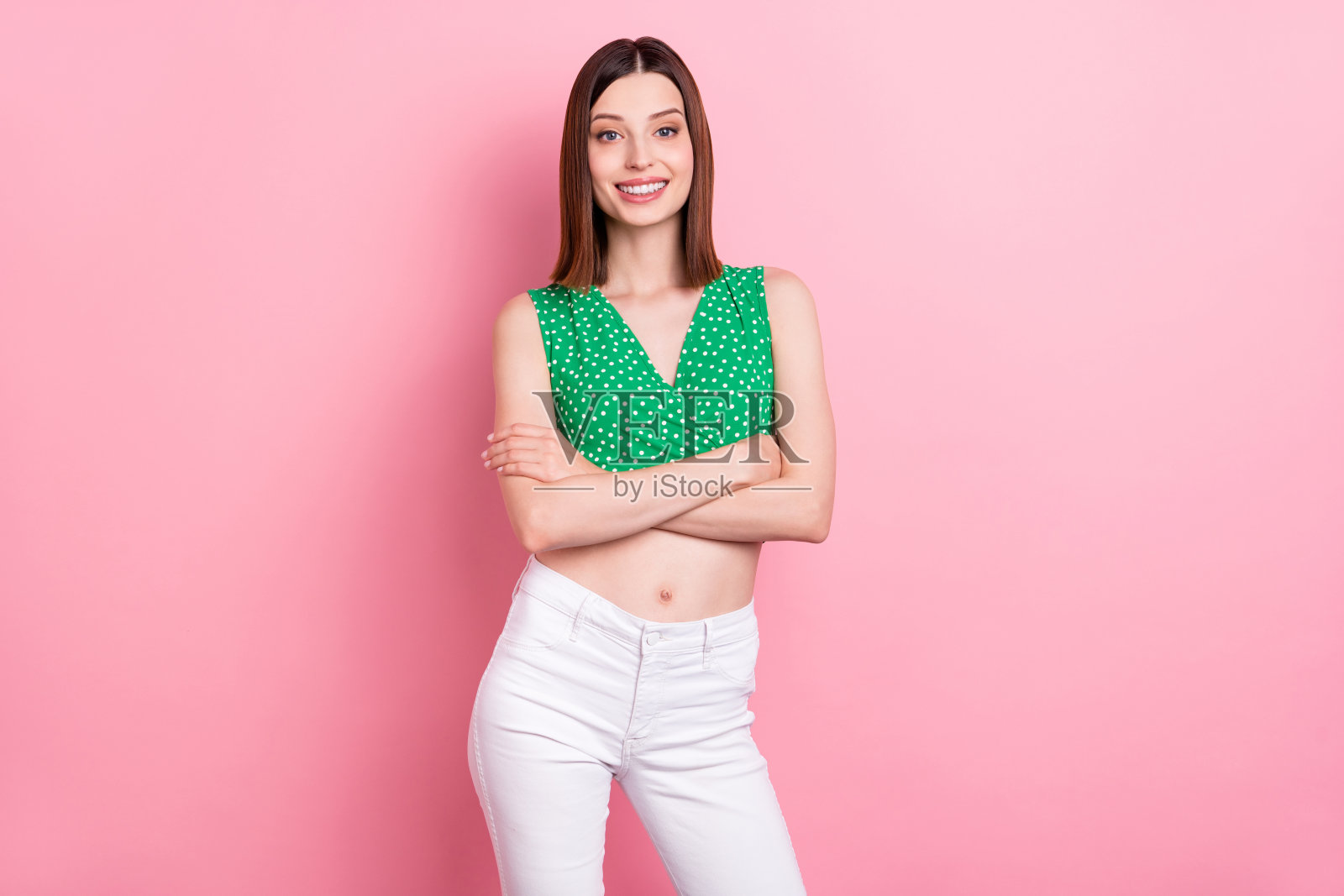 青春洋溢的女孩自信地交叉双手，穿着现代服装，背景为粉色。照片摄影图片