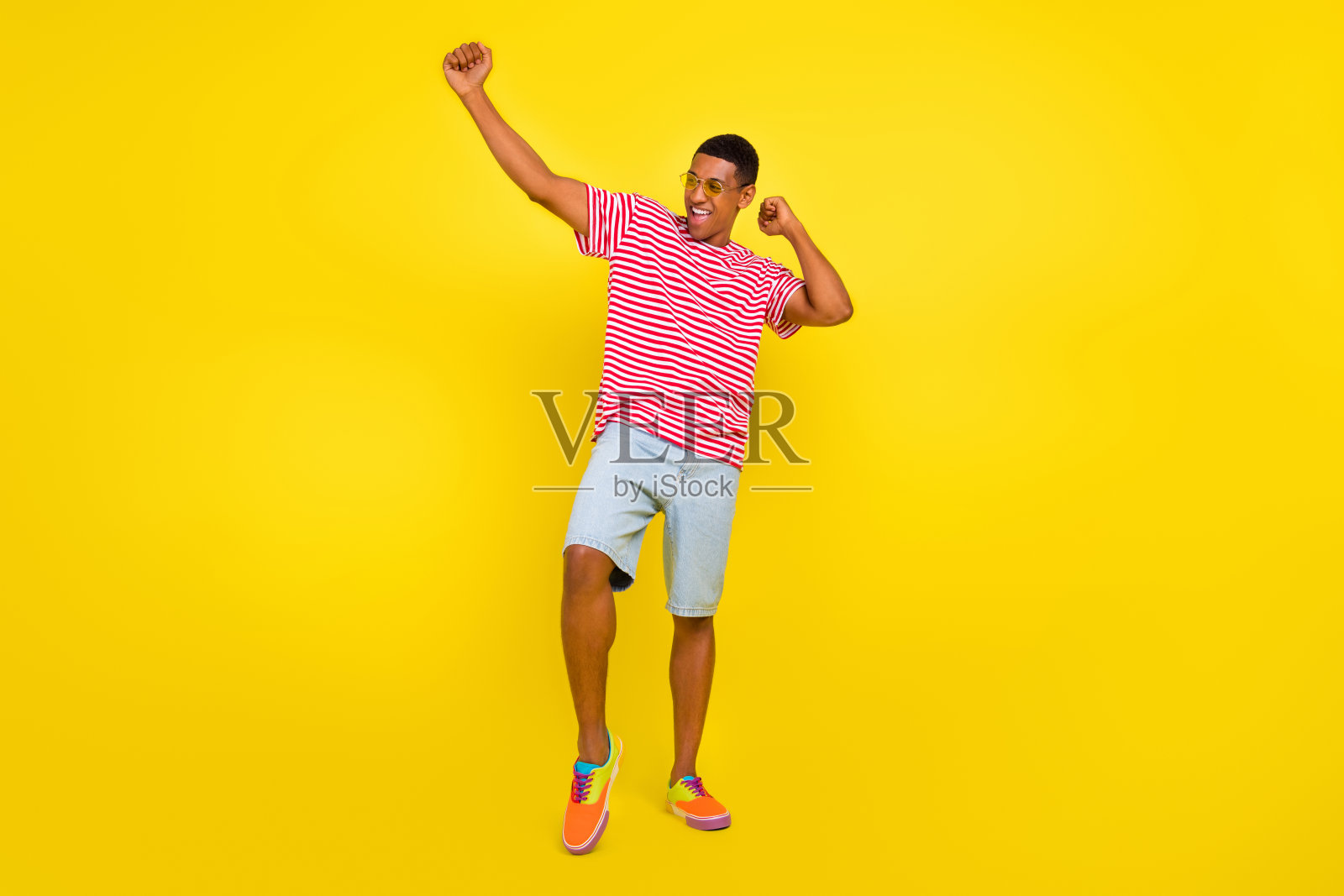 全身照，充满活力的男孩跳舞，举起拳头，穿着红色条纹衣服，背景为明亮的黄色。照片摄影图片