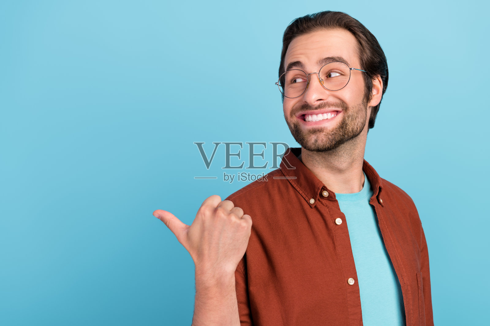 一位令人印象深刻的棕发千禧一代男士，穿着时尚的眼镜服装，独自站在蓝色背景前。照片摄影图片