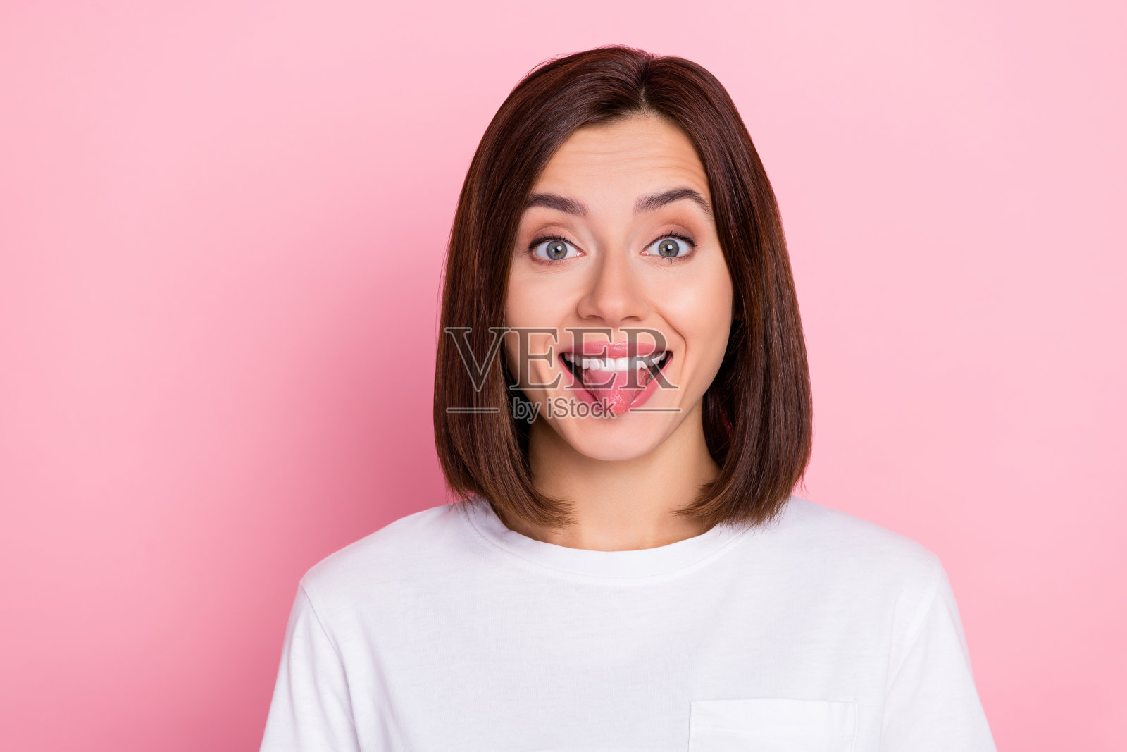 一位迷人的时尚女士在粉色背景下调皮地吐舌头，表现出无忧无虑的行为。照片摄影图片