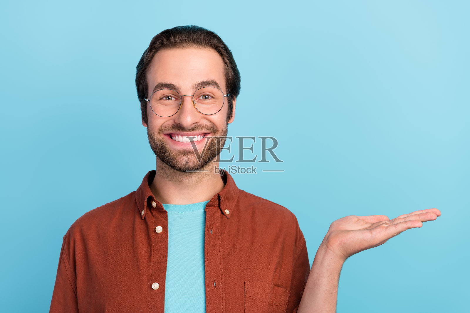 一位棕发的千禧一代男性CEO穿着促销服装，戴着眼镜，独自站在蓝色背景前。照片摄影图片