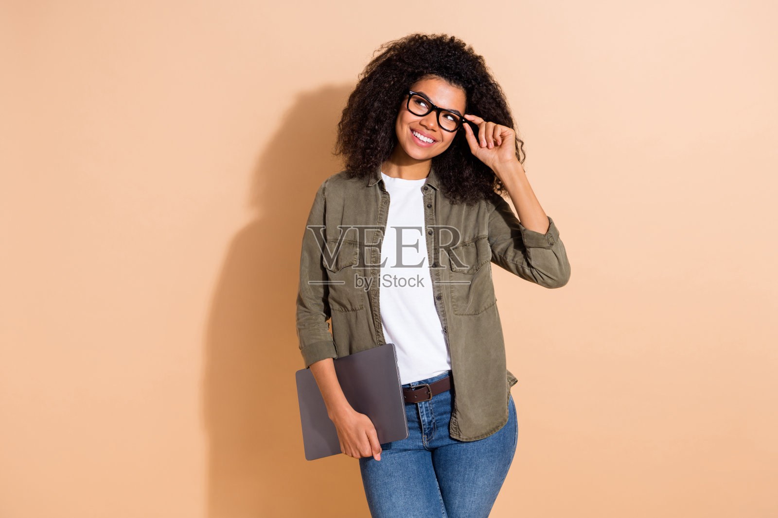 年轻可爱的好奇女孩凝视空旷的空间，思考梦幻的创意项目，坐在笔记本电脑前，背景为米色。照片摄影图片