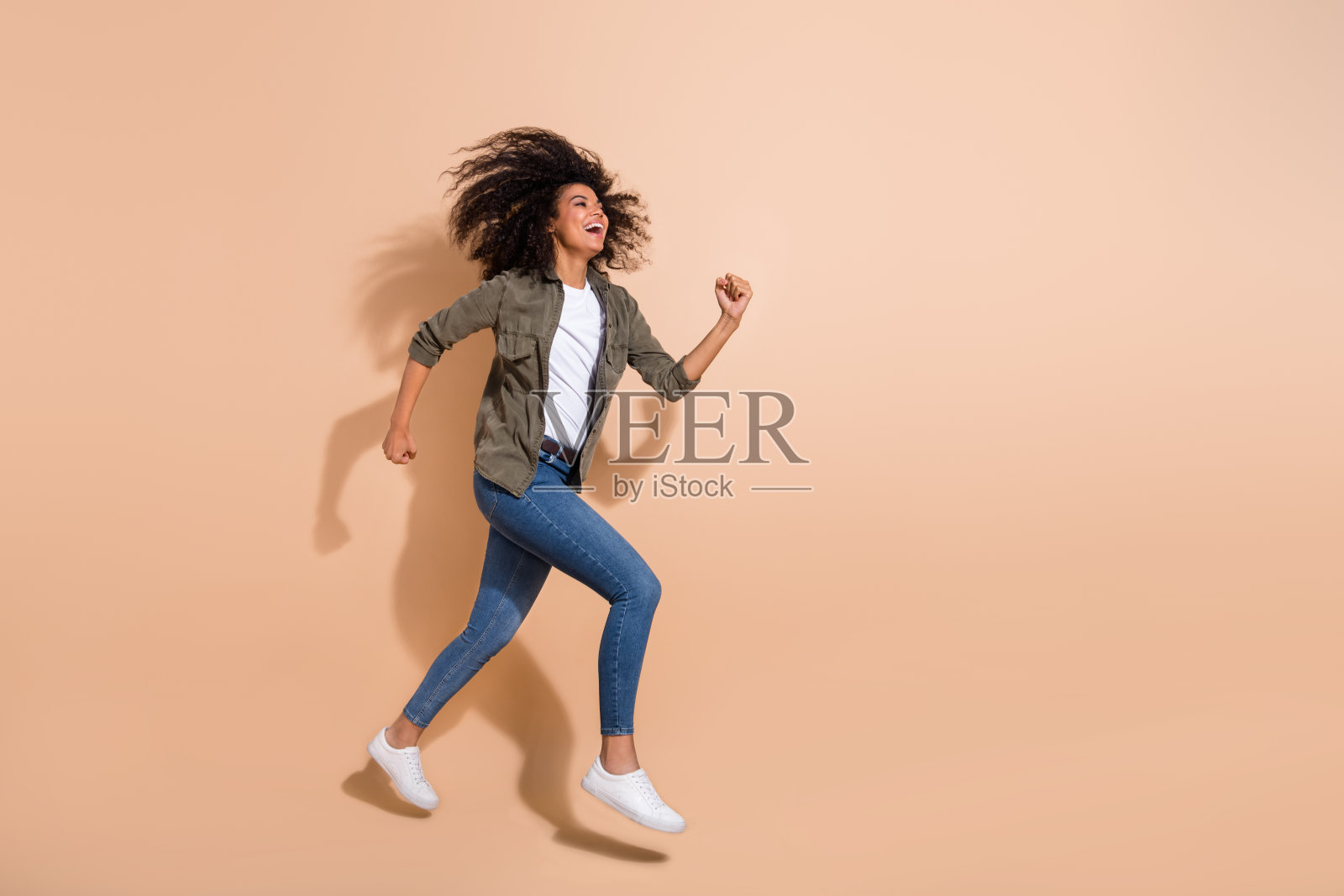全身视角的漂亮快乐女孩在米色柔和背景上跳跃奔跑，尽情享受。照片摄影图片