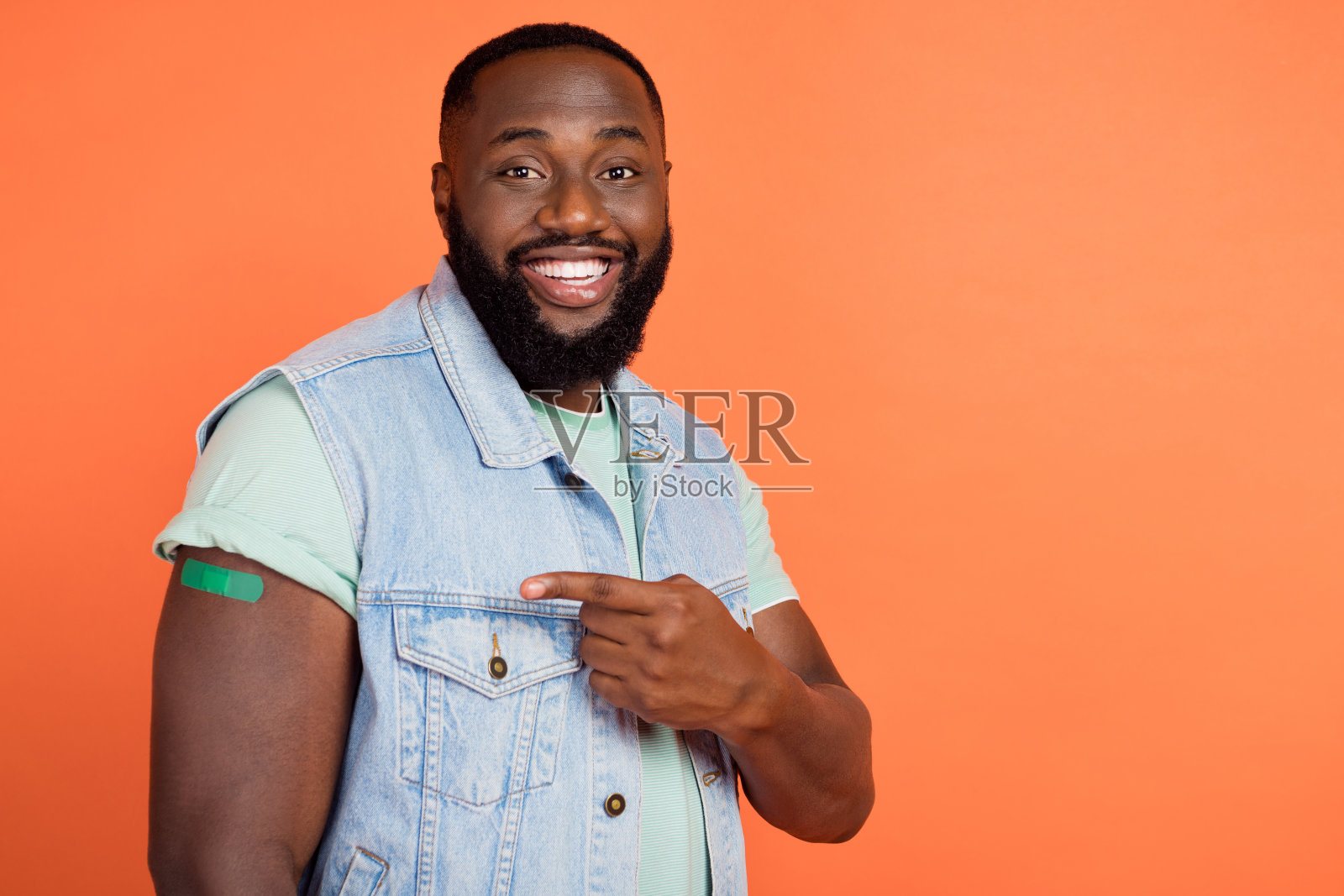 兴奋的非洲裔男士穿着牛仔背心，指着空白处的创可贴，背景为橙色。照片摄影图片