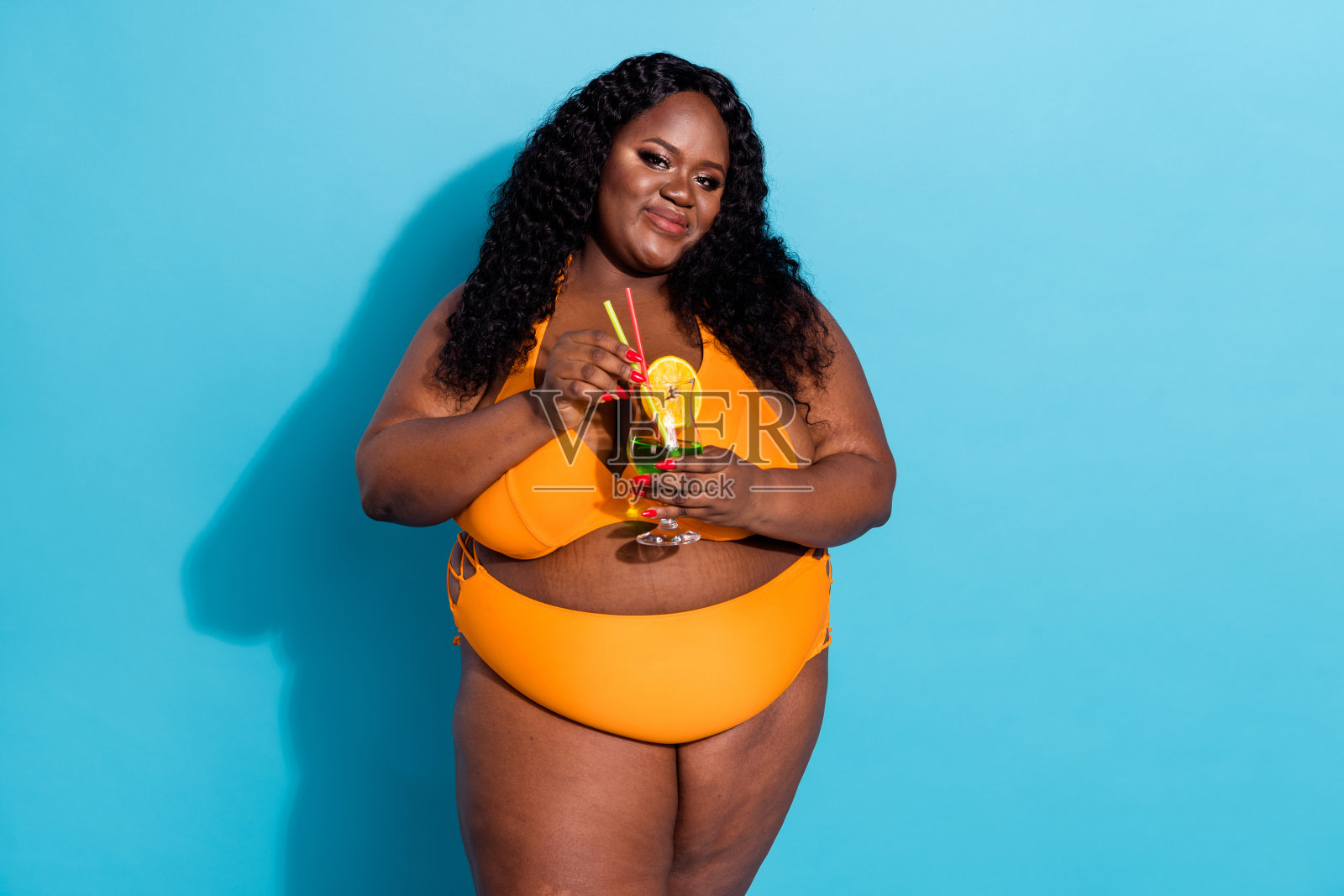 美丽迷人的女士手持饮料杯，享受自我，无滤镜，背景为蓝色。照片摄影图片