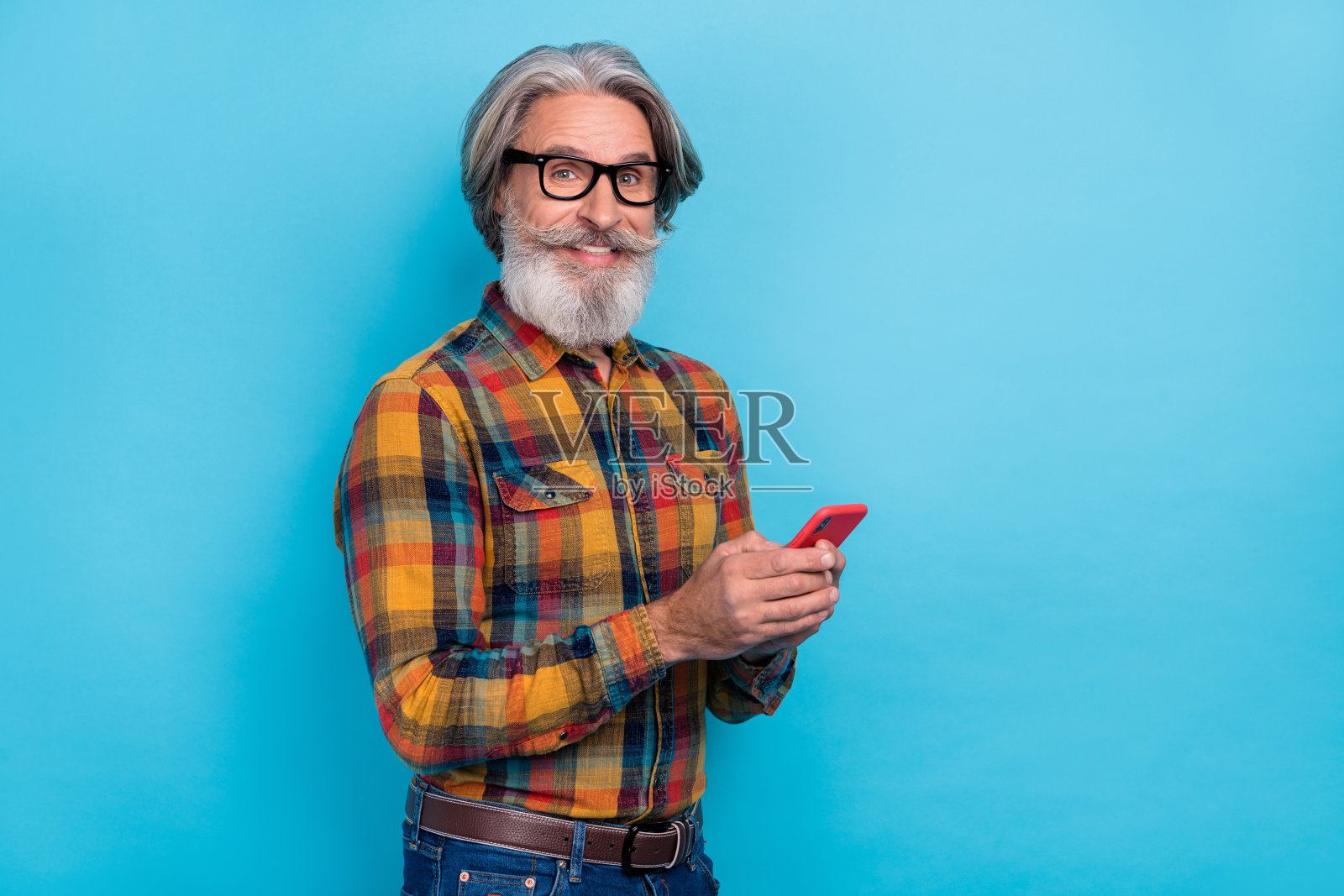 老年男性侧面肖像，使用手机发送短信，转发、订阅、聊天、点赞和评论，背景为蓝色。照片摄影图片