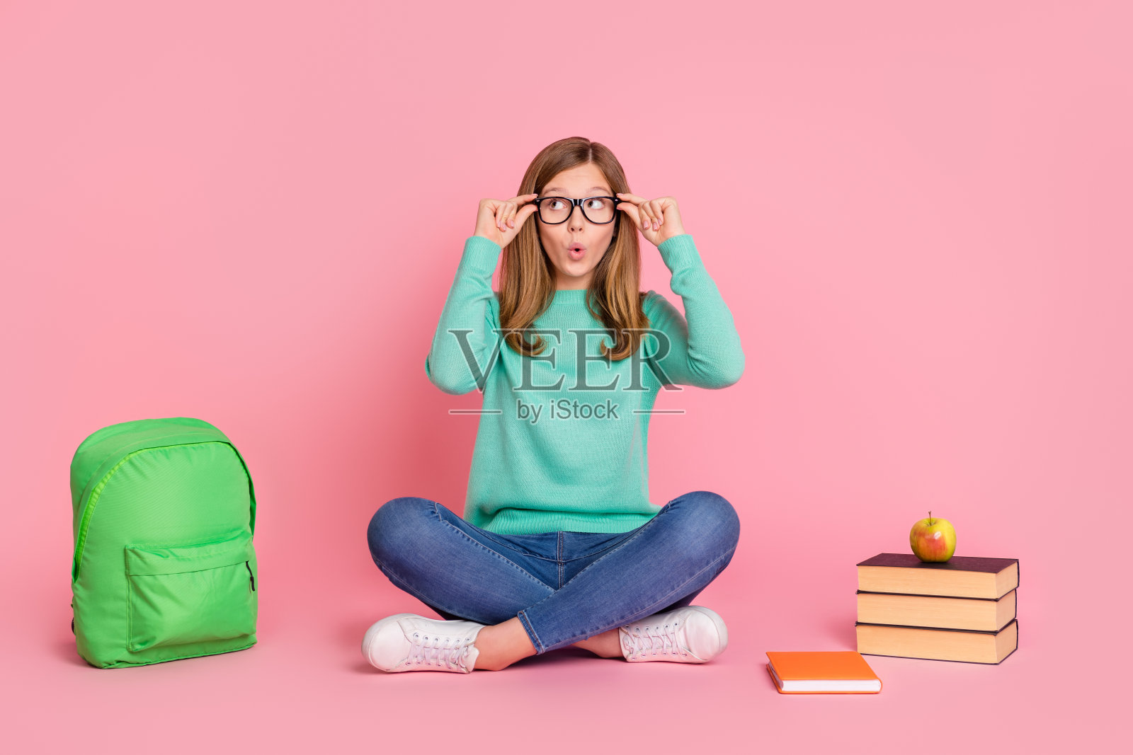 穿着青色毛衣、戴着眼镜的印象深刻的女学生，手里拿着文具，目光空洞，背景为粉色。照片摄影图片