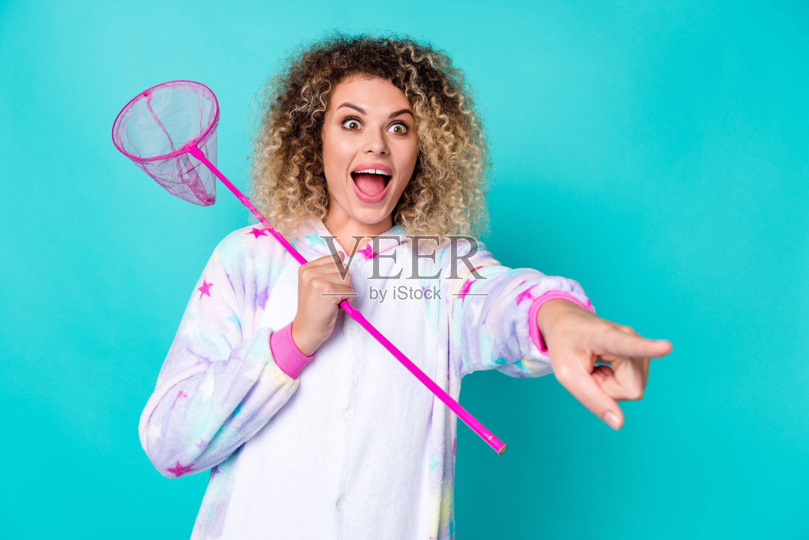 穿着睡衣的兴奋女士在空旷的地方指着捕捉昆虫，背景为青绿色。照片摄影图片