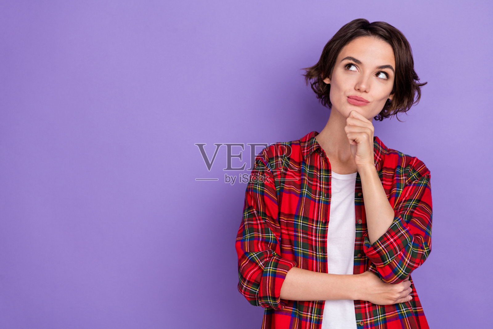 思考的年轻短发女士穿着红色衬衫，背景为紫色。照片摄影图片