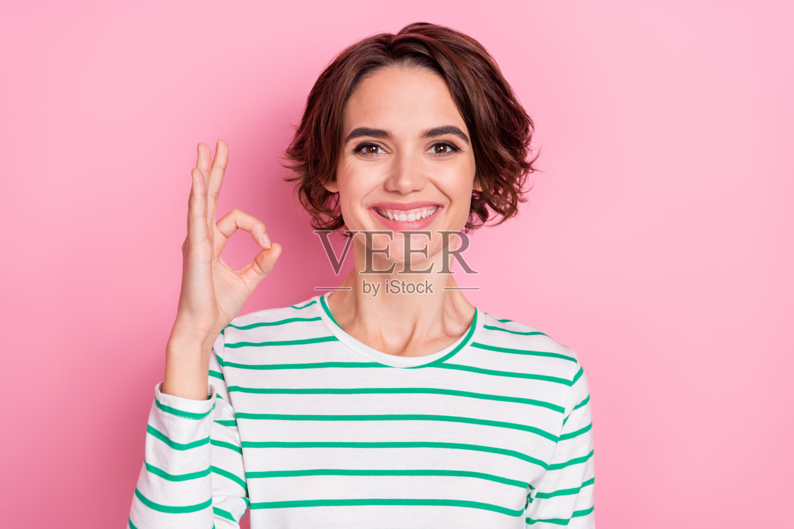 迷人的快乐棕发女孩在粉色背景上做出“好”的手势，表示同意和广告解决方案。照片摄影图片