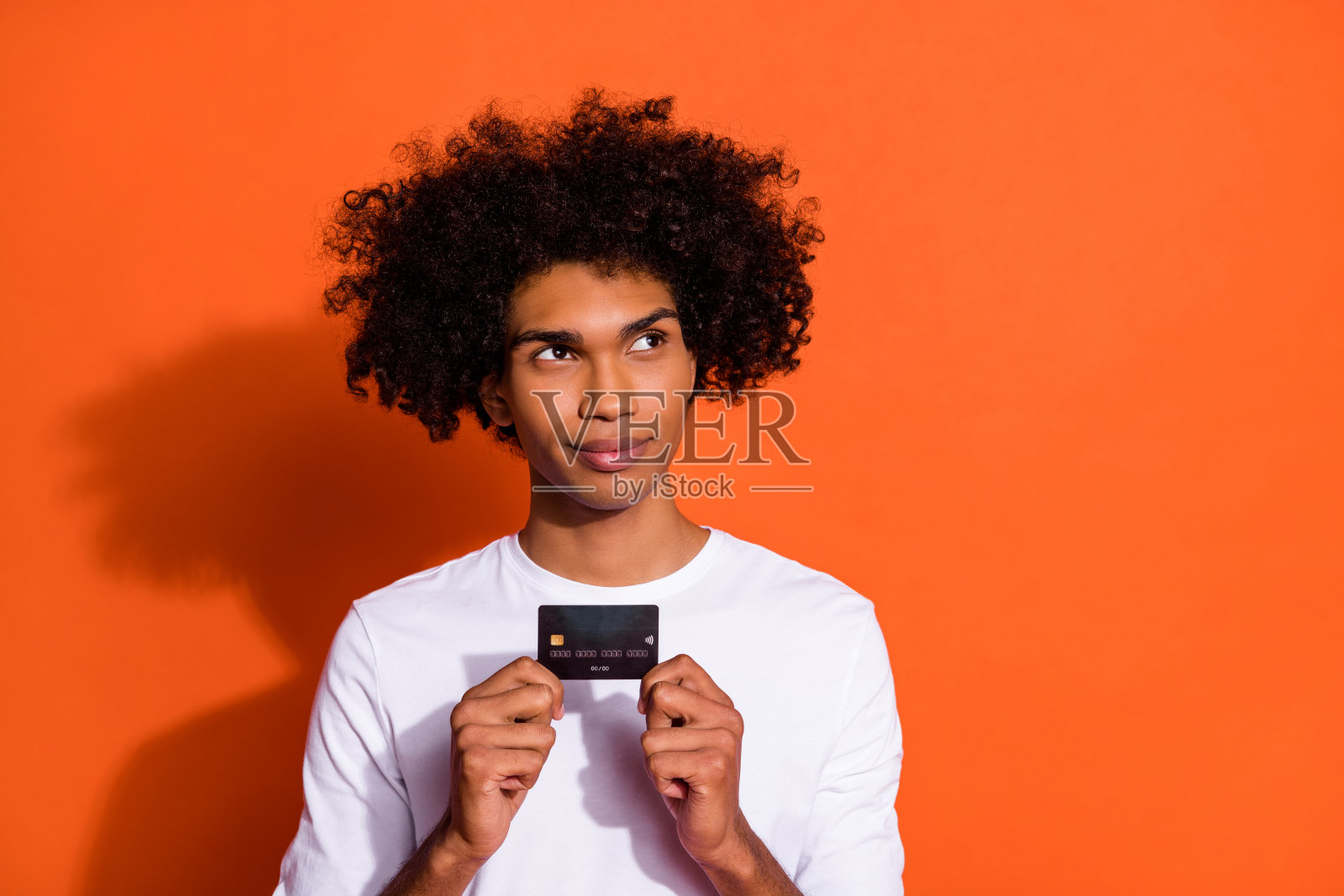 穿着白衬衫的帅气怀疑男士手持信用卡，背景为橙色，空白区域可供使用。照片摄影图片