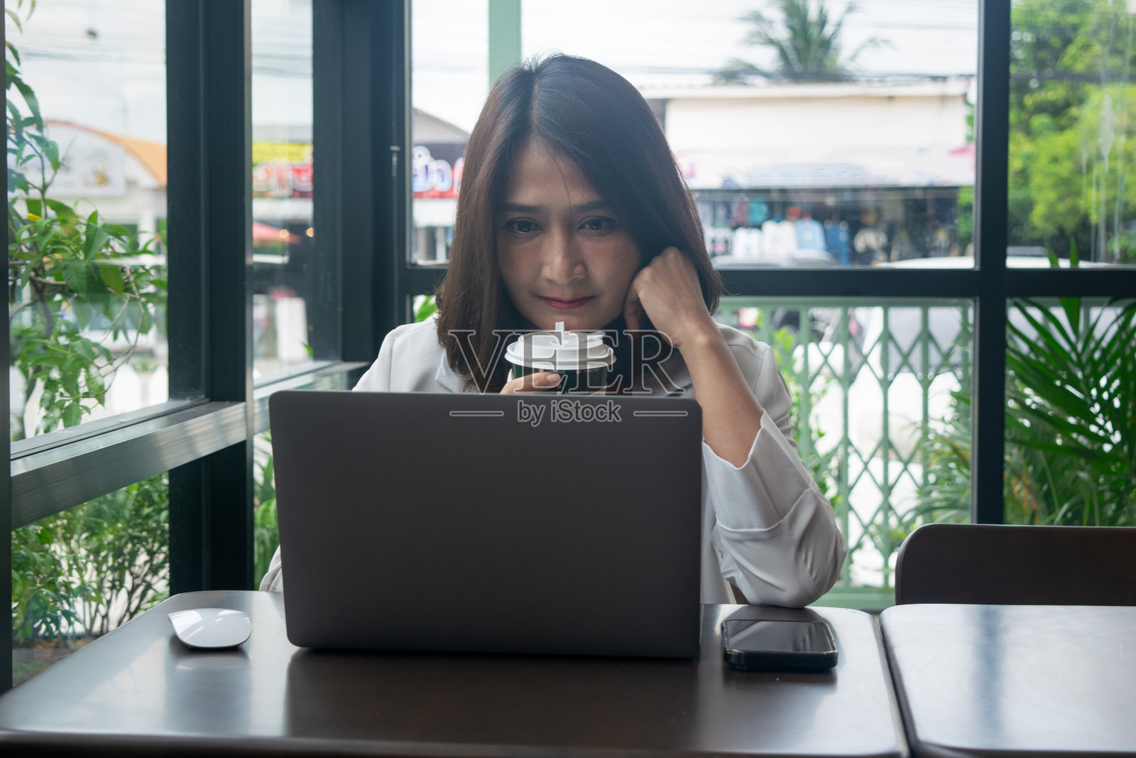 女商人在咖啡馆里手握咖啡杯，使用笔记本电脑处理财务工作报告，展现自由职业者的商业理念。照片摄影图片