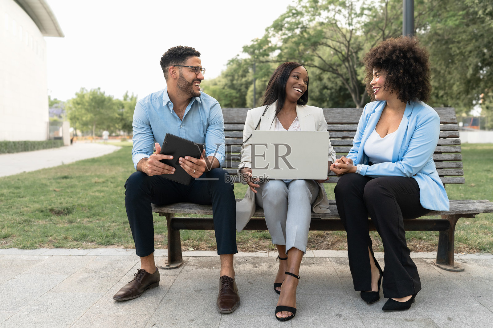 多元种族的商业团队坐在城市公园的长椅上，讨论新项目并使用笔记本电脑。照片摄影图片