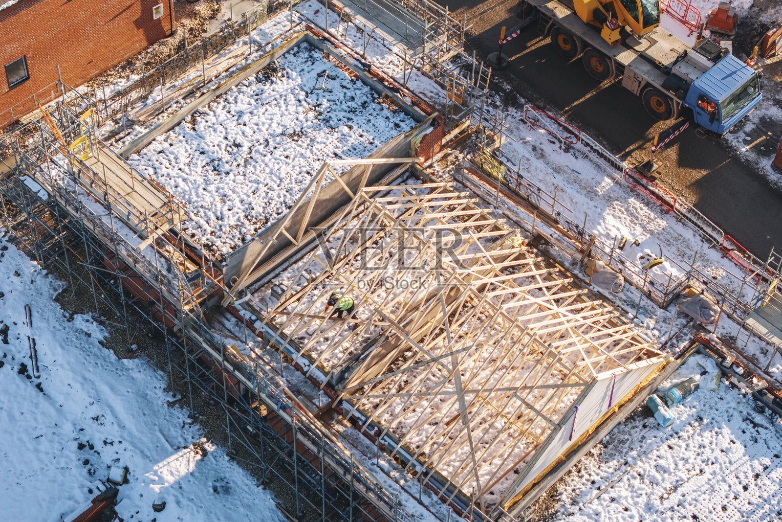 冬季雪覆盖地面的建筑工地鸟瞰图，黄色移动起重机和脚手架。照片摄影图片