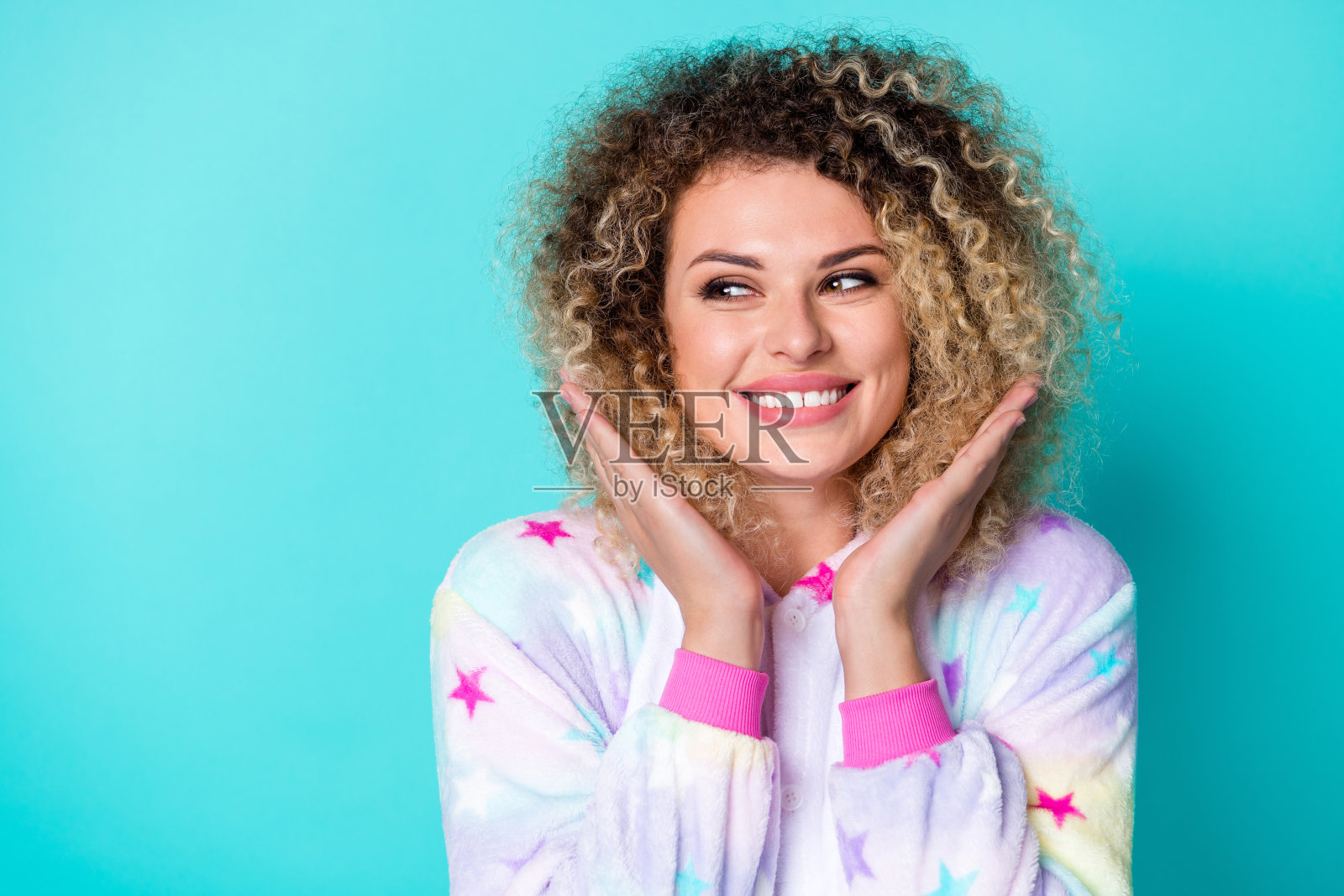 穿着睡衣的漂亮千禧一代女士，手托着脸，卷发造型，背景为蓝色。照片摄影图片