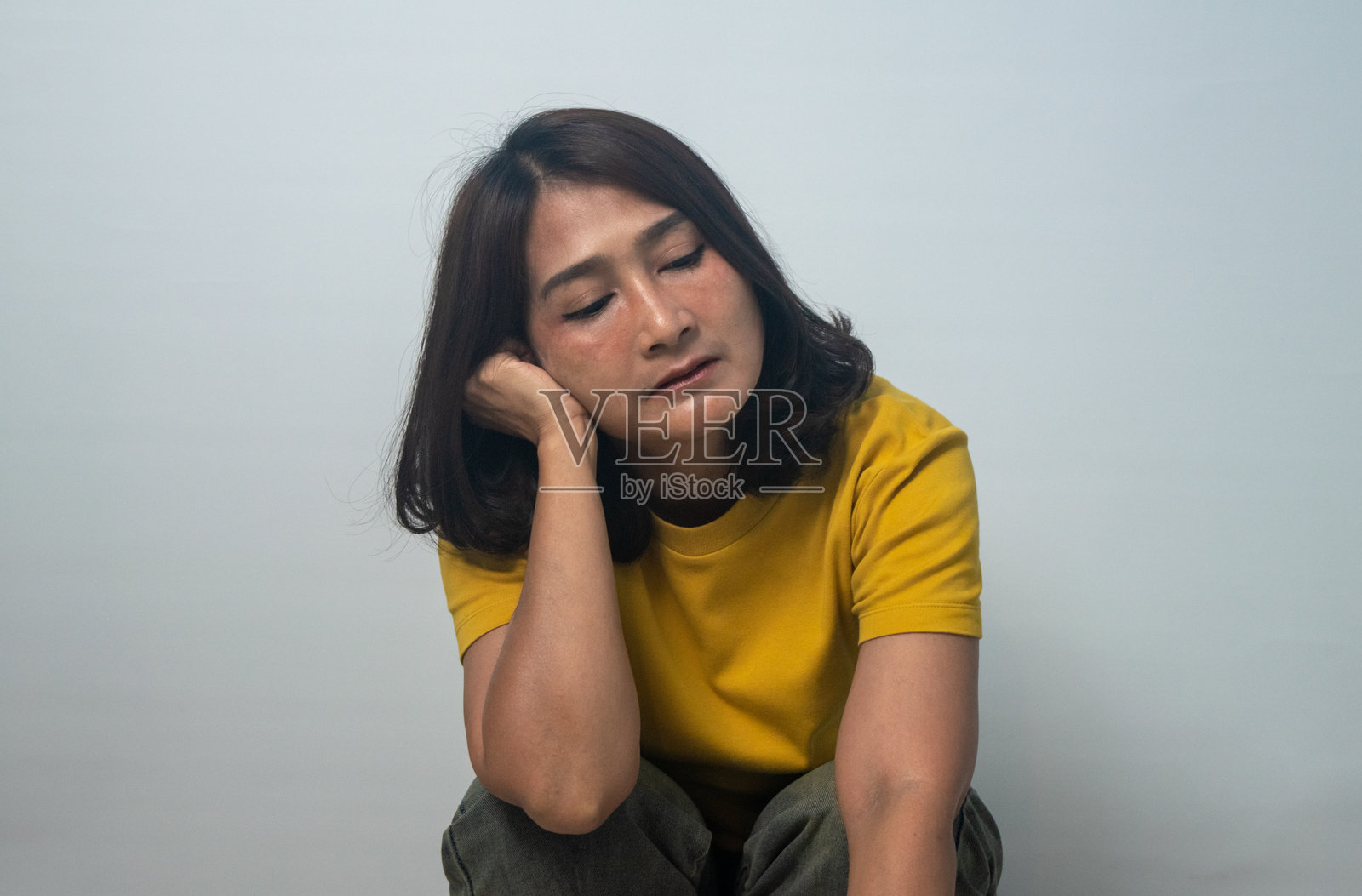 穿着黄色衬衫的亚洲女性坐在地板上，手臂搭在膝盖和头上，面露绝望、悲伤、困扰和孤独，表情震惊，显得焦虑和疲惫。照片摄影图片