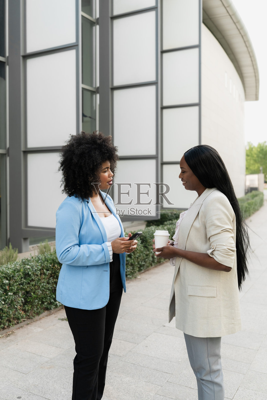 两位多种族的女商人在办公楼外边喝咖啡边交谈照片摄影图片