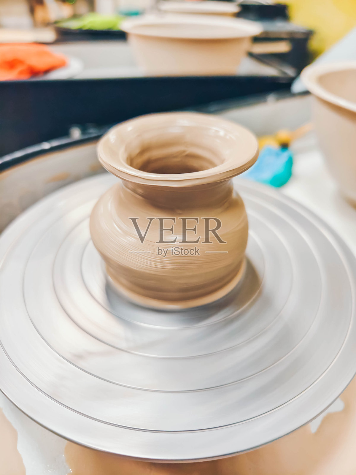 陶土碗在旋转的陶艺轮上。制作陶瓷花瓶。照片摄影图片