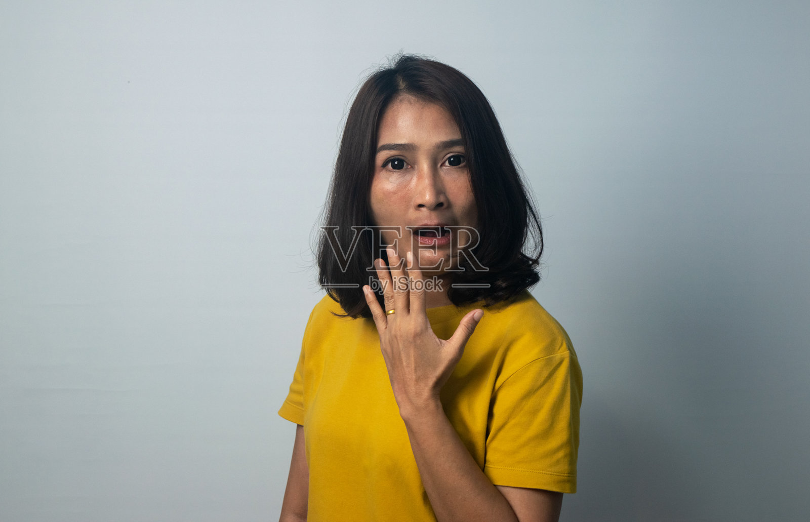 亚洲女性站在灰色背景前，眼睛大睁，惊讶地张嘴，面露震惊的表情，既害怕又兴奋地看着镜头。照片摄影图片