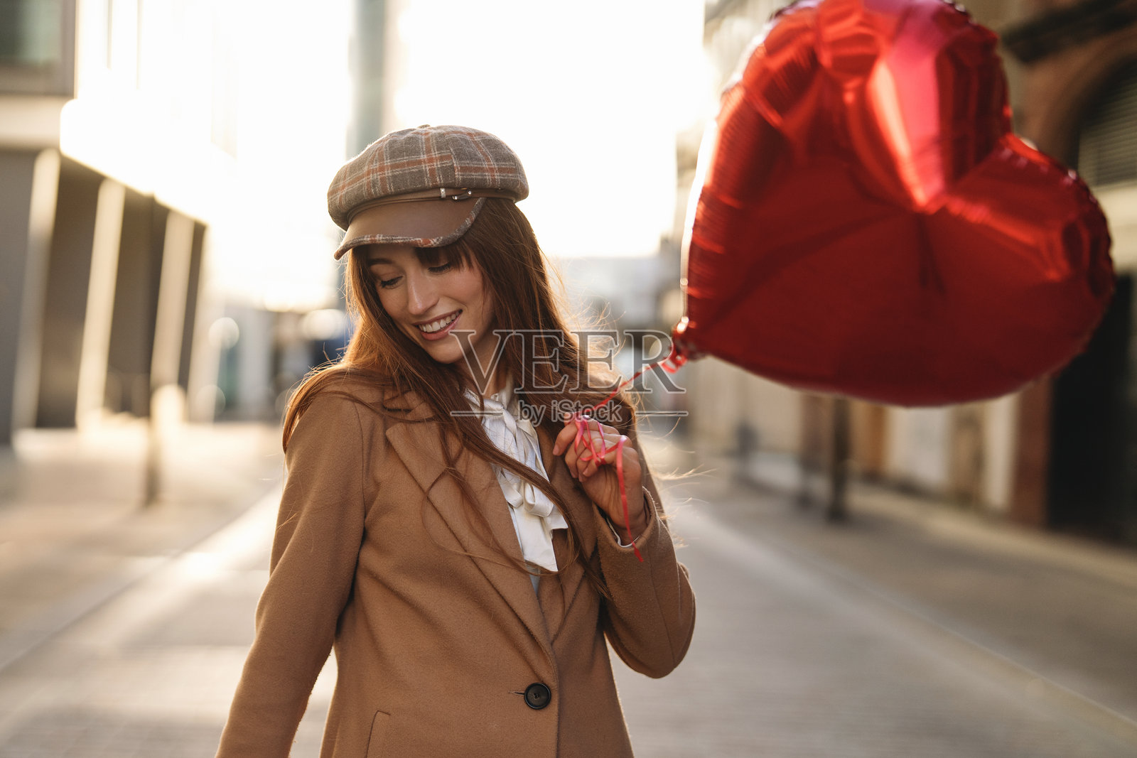 年轻女性在城市中享受阳光明媚的一天，手持心形气球，穿着时尚，展现出愉快的神情照片摄影图片