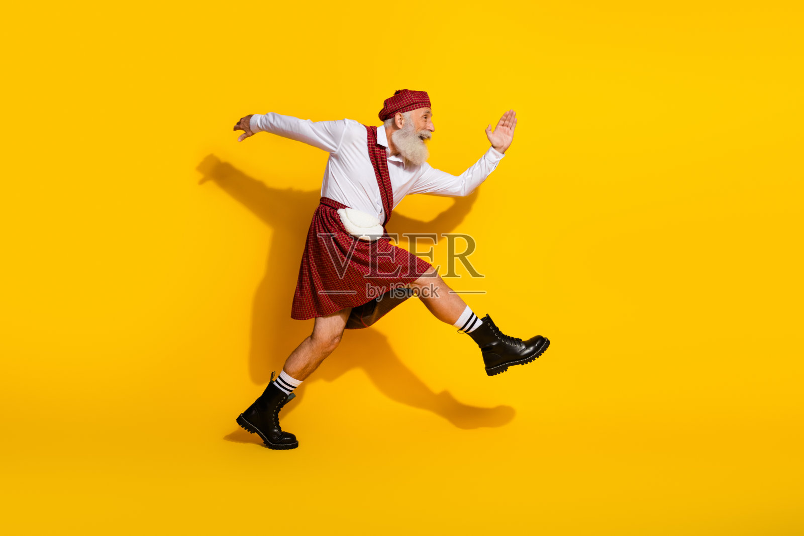 身穿传统苏格兰服饰的老人愉快地在明亮的黄色背景上迈步，彰显出丰富的文化和快乐。照片摄影图片