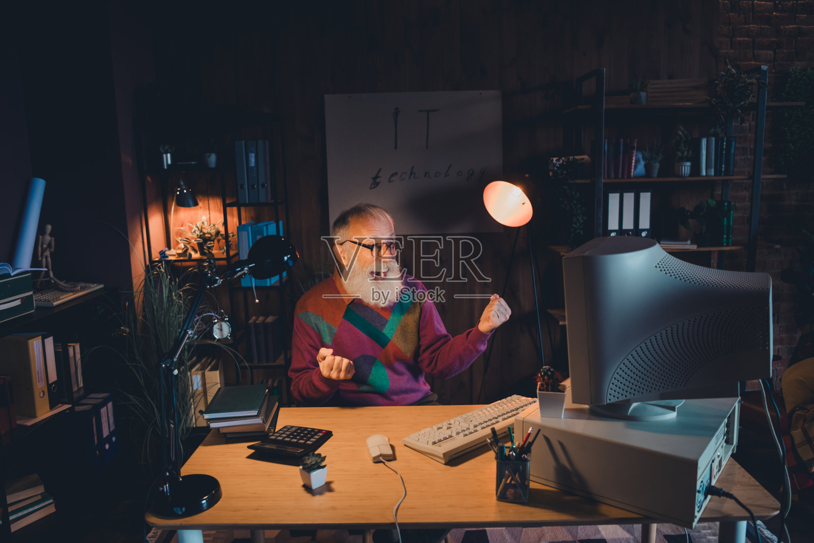 在温暖灯光照耀下，老年男性程序员在家中办公室工作。照片摄影图片