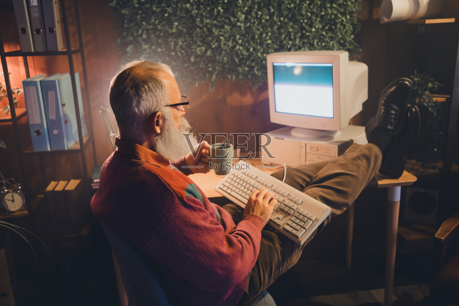 成熟的白胡子男人在舒适的家居办公室里工作，喝着咖啡，环境充满复古风格。照片摄影图片