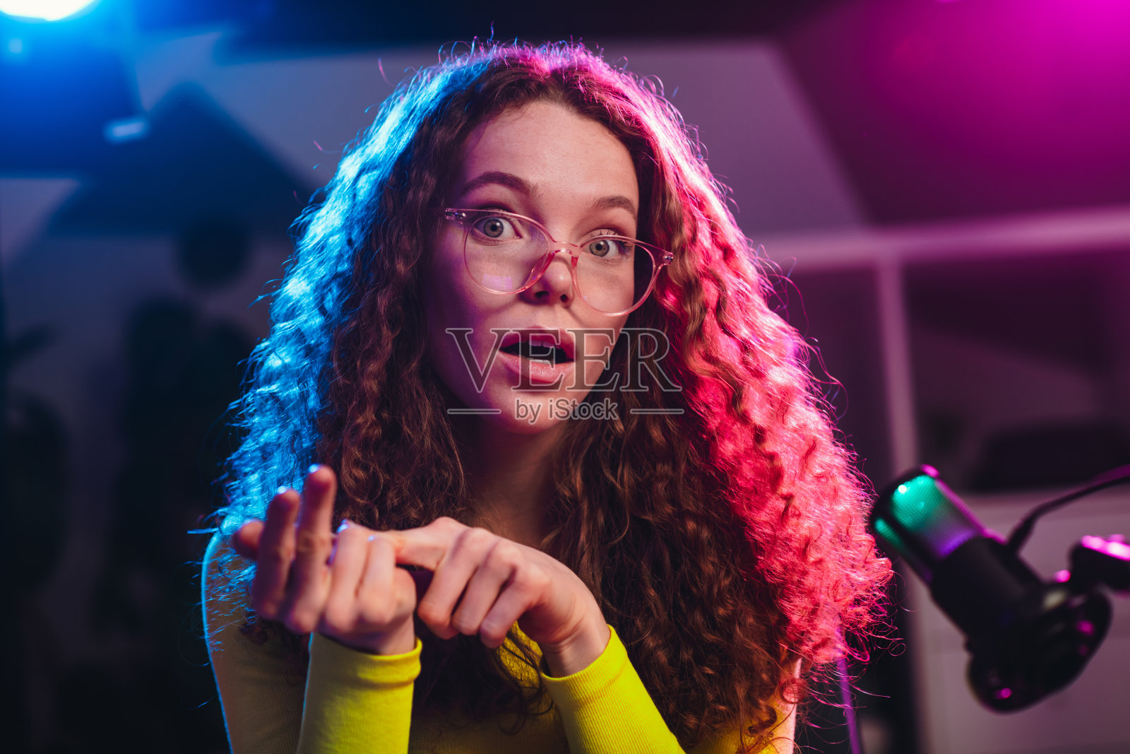 迷人的女孩，卷发戴着眼镜，在五光十色的霓虹灯下夜间直播。照片摄影图片