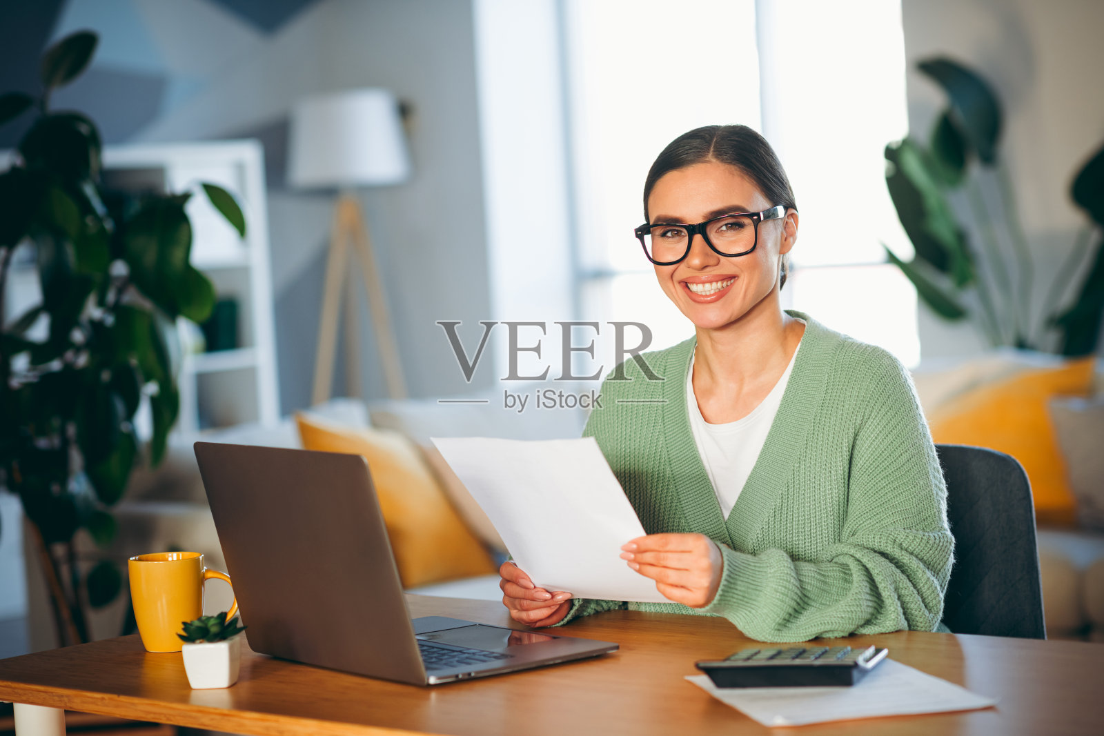 微笑的年轻女性在舒适的客厅中使用笔记本电脑和文件远程工作，享受着平衡的生活方式照片摄影图片