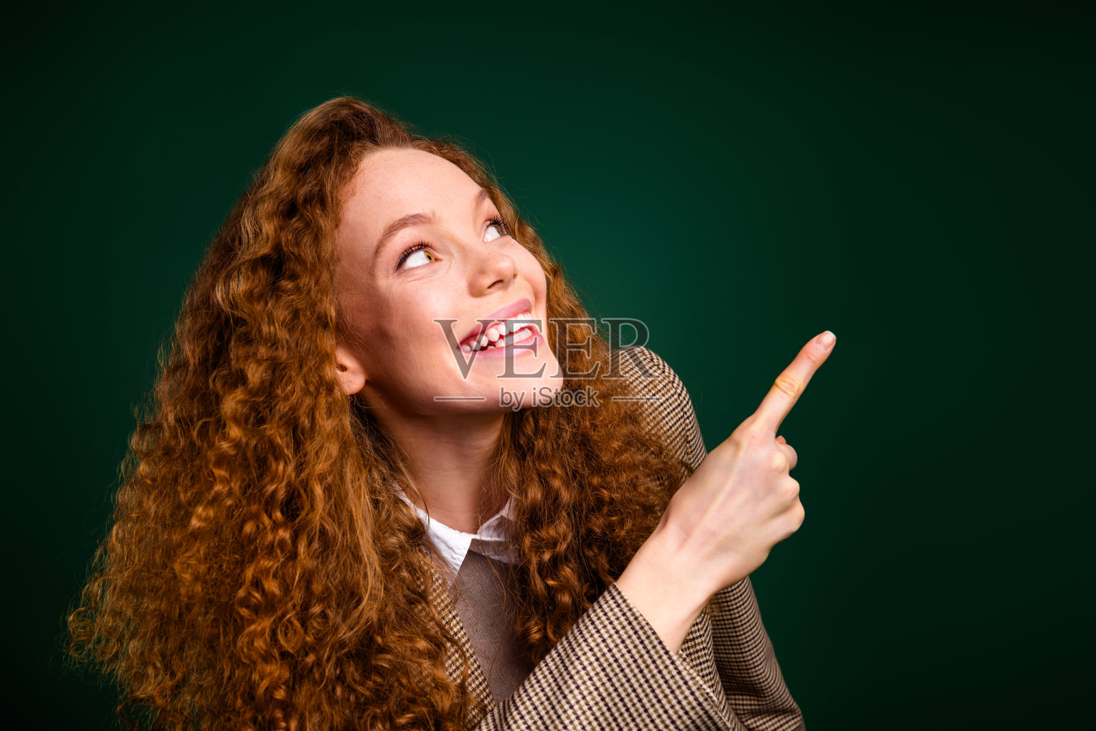 微笑的卷发女商人用手指向上方，背景为绿色。照片摄影图片