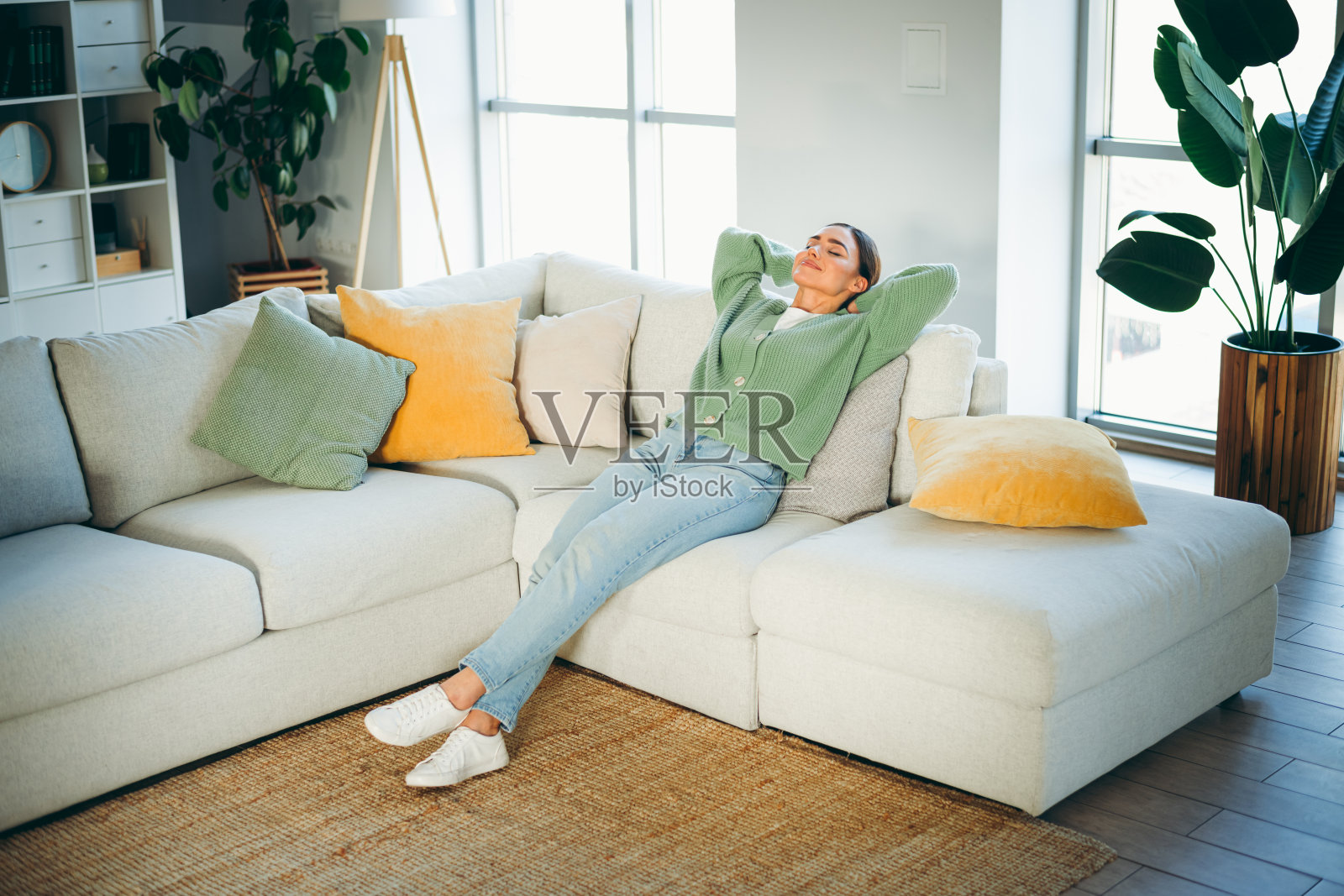 年轻女性在明亮的客厅里的舒适沙发上放松，享受周末下午的家庭舒适和休闲时光照片摄影图片