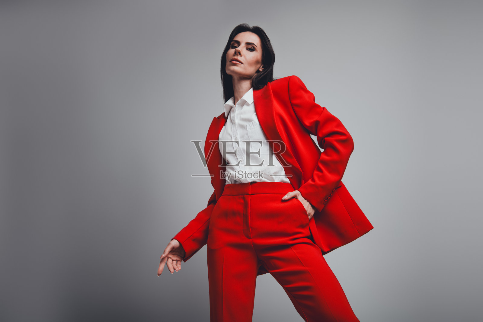 自信的女商人在中性色背景下展示风格与优雅，身穿鲜艳的红色正装。照片摄影图片