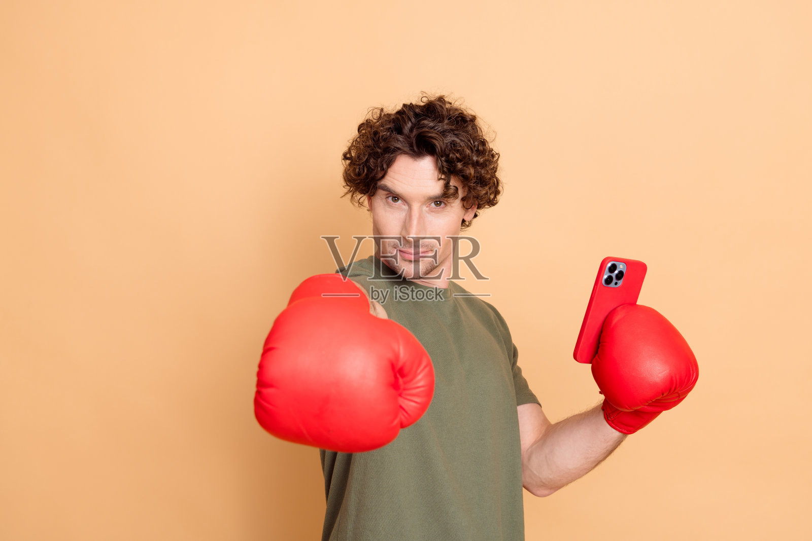 年轻的卷发男士戴着红色拳击手套，手持智能手机，展现出自信与风格。照片摄影图片