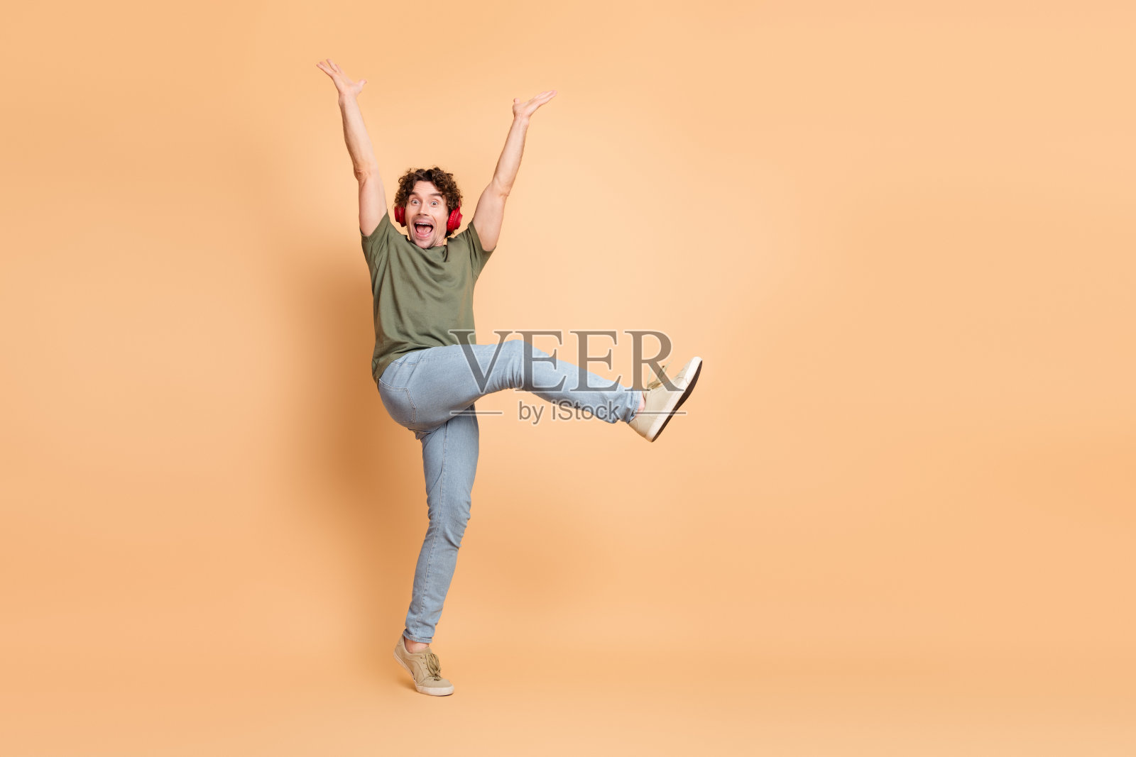 穿着休闲服的年轻男子在中性米色背景前欢快地跳跃，表达兴奋之情照片摄影图片