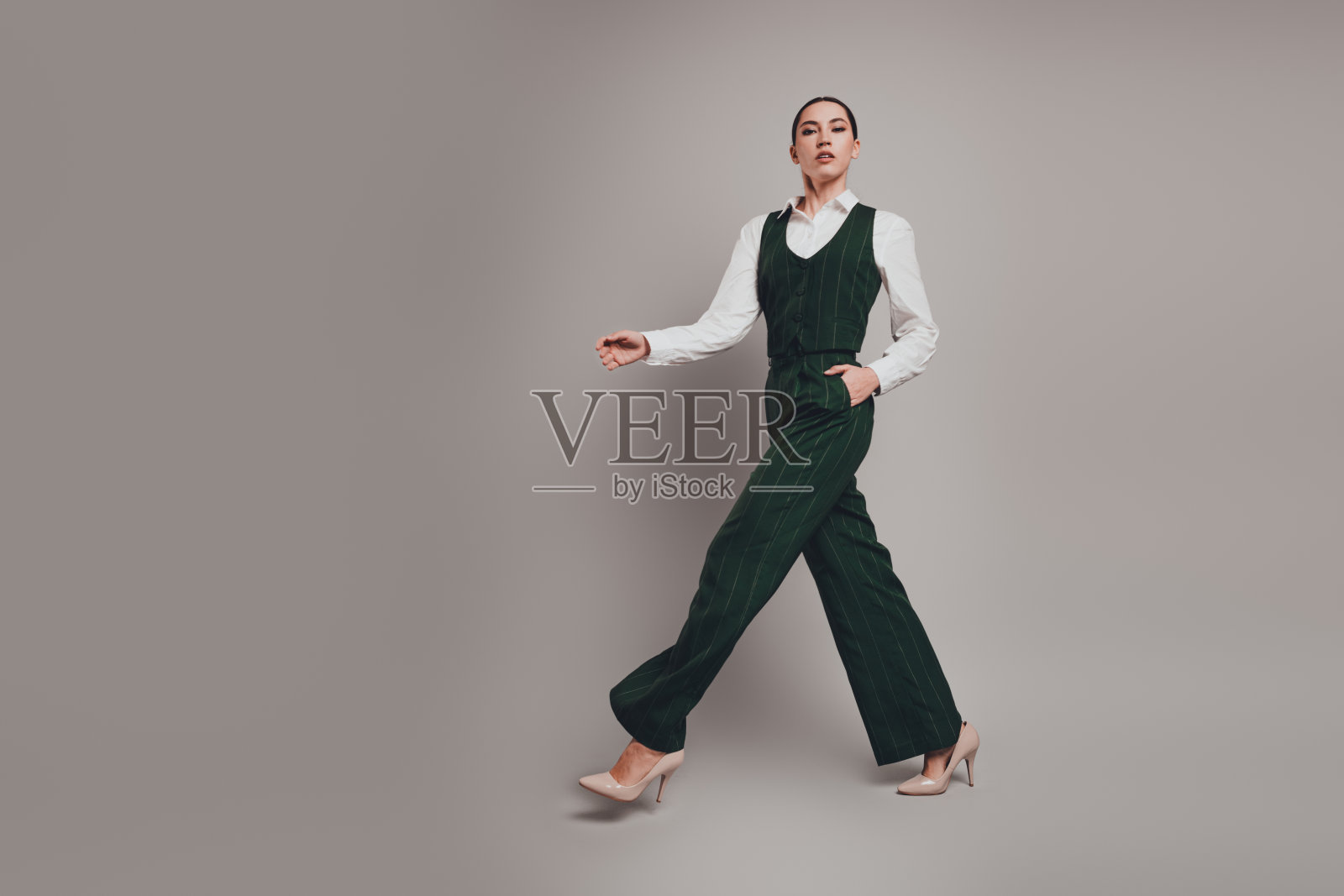 自信的女商人在优雅的绿色西装中，优雅地走过灰色背景。照片摄影图片
