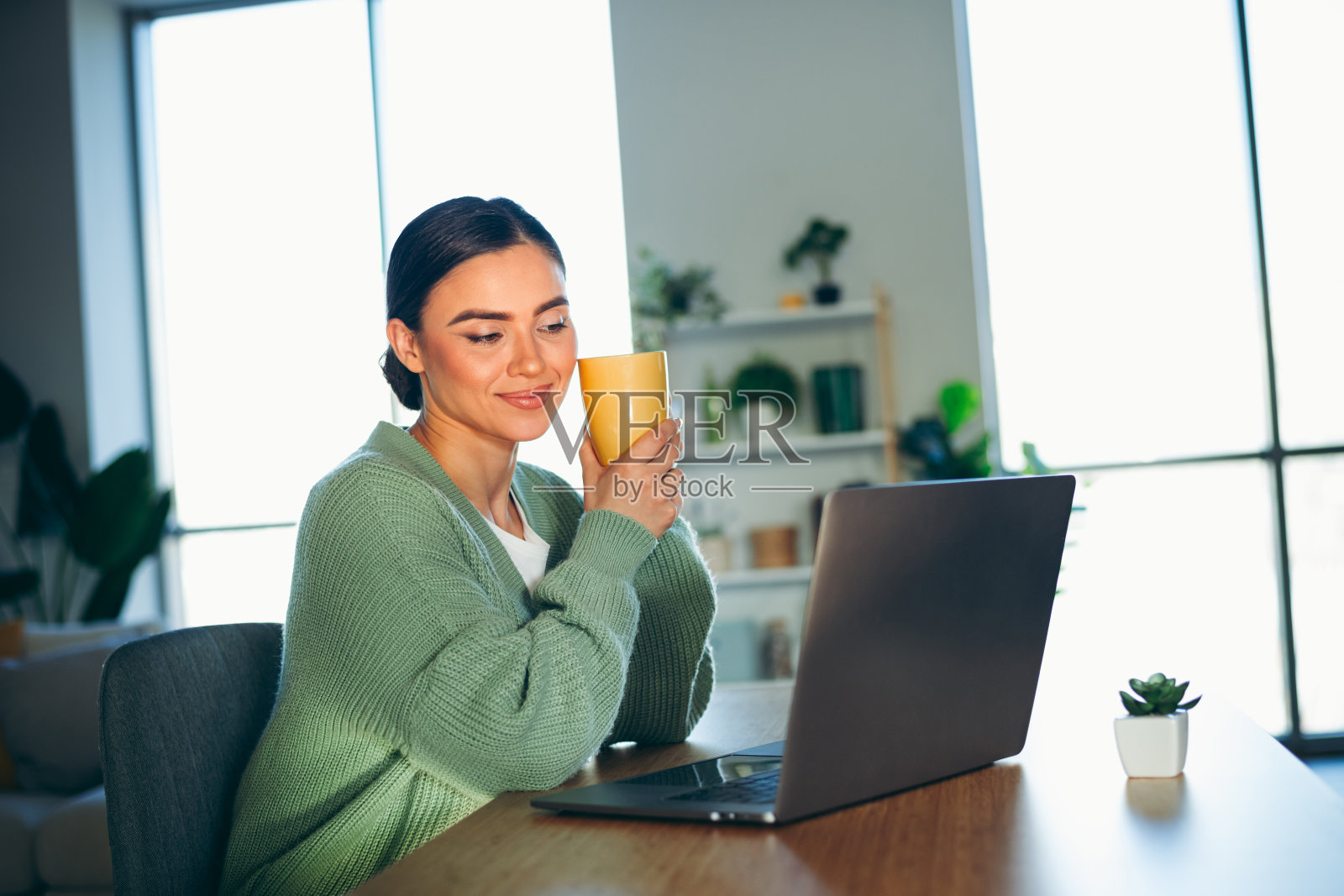年轻女性在室内享受轻松的一天，手握热饮和笔记本电脑，拥抱舒适惬意的生活方式照片摄影图片