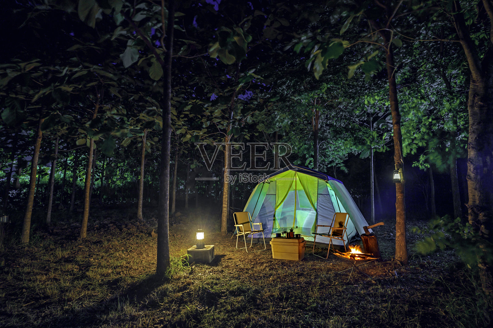 夜间的露营帐篷，复古的小木屋帐篷，古董灯笼，复古椅子，以及森林中木桌上的户外咖啡制作设施照片摄影图片